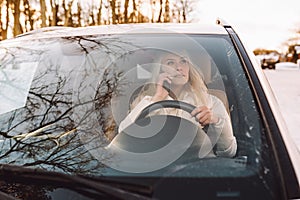 Blonde young woman drive white car while talking by phone and looking at side.