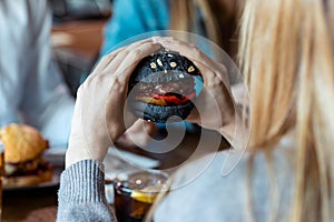 Blonde young woman eating delicious burger while having fun with her friends in the restaurant