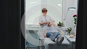 Blonde young woman getting facial massage with a jade roller in beauty spa salon