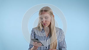 Blonde young woman holding her chin with hand while thinking about something on blue background.