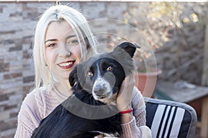 Blonde young woman hugging her dog while sitting outdoors in a terrace