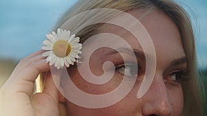 Blonde young woman puts a chamomile on her ear