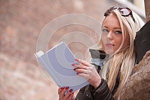 Blonde young woman reading a book outdoors