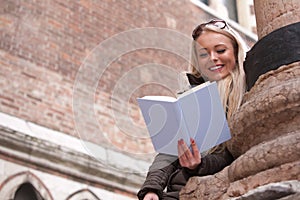 Blonde young woman reading a book outdoors