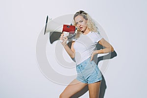 Blonde young woman shouting with a megaphone isolated on a white background