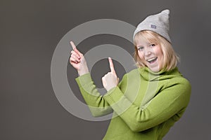 Blonde young woman smiling broadly at camera, pointing fingers away, showing something interesting