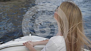 Blonde young woman in sunglasses sails in boat on dark water