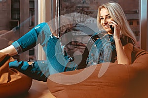 Blonde young woman talking phone and smiling on camera in casual