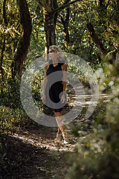 Blonde young women in a black dress with a hood walks in a mysterious forest