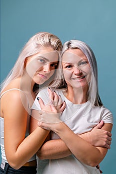 Blondehaired Mom and teenager daughter smiling on colorful backgroung. Middle studio shoot with copy space photo