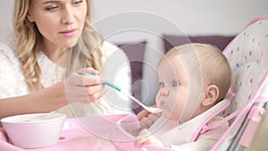 Blondy woman feeding child with spoon. Mom feed baby with pureed food
