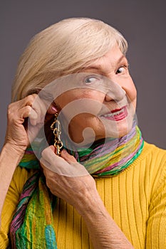 Blone smiling senior woman putting on long earrings