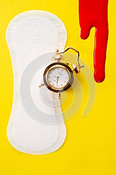 Blood, alarm clock and feminine hygiene pad with red glitter on yellow background. First menstrual period concept