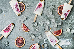 Blood orange, yogurt and granola popsicles on ice, grey background