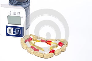 Blood pressure checker and colorful tablets arranged in heart shape