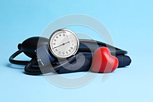 Blood pressure meter and toy heart on light blue background