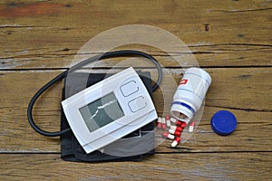 Blood pressure monitor and pot with medicine capsules on wooden background