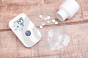 blood pressure monitor and white jar with tablets on a wooden background, heart made of white powder, pulse drawn