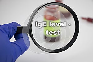 A blood sample for a test for immunoglobulin IgE level. The doctorÃ¢â¬â¢s hand holds a magnifying glass in which a test tube with a photo