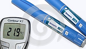 Blood sugar meter with test strips indicates high blood sugar levels and Ozempic injection pen for diabetes.