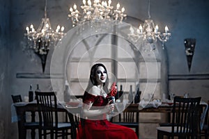 Bloodthirsty female vampire in red dress. Medieval interior