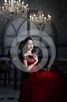 Bloodthirsty female vampire in red dress. Medieval interior