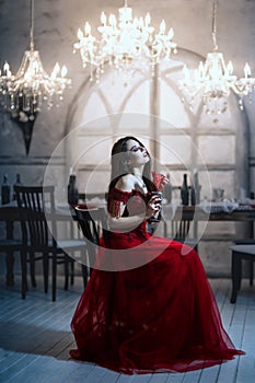 Bloodthirsty female vampire in red dress. Medieval interior