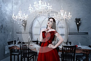 Bloodthirsty female vampire in red dress. Medieval interior photo