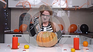 Bloodthirsty young woman in Halloween skeleton costume laughs viciously and insidiously strokes pumpkin, sticks knife