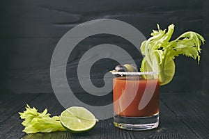 Bloody mary cockCocktail Bloody Mary with lime and celery, salt and snacks in a glass on a black wooden table. horizontal view of