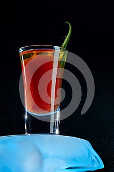 Bloody Mary cocktail close-up, decorated with greenery, standing on an ice floe on a dark background with a snow haze