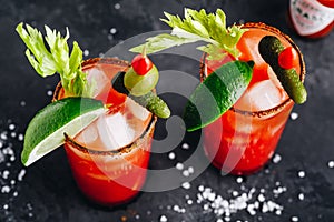 Bloody Mary Cocktail in glasses with garnishes. Tomato Bloody Mary ice cold drink with fresh celery, pickles and lime