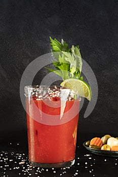 Bloody Mary cocktail with tomato juice, lime, and celery, wiuth pickles, side view on a black background