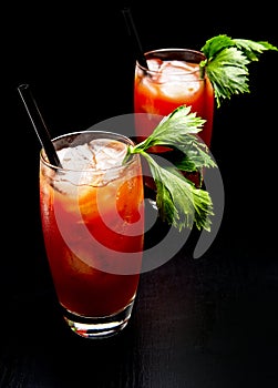 Bloody Mary cocktails with ice cubes and celery isolated on black