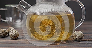 Blooming flower tea ball brewing in a glass teapot with Hot boiling water on wooden background