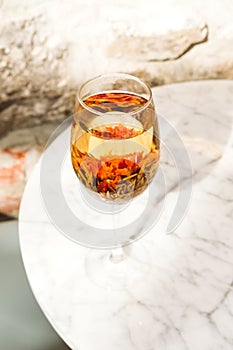 Blooming flower tea served in a wine glass, white marble table at the trendy cafe
