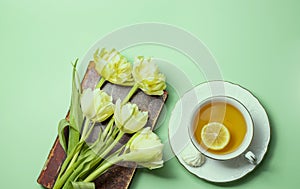 Blooming Saintpaulia, commonly known as African violet, cup of tea with lemon, vintage book close-up. Composition for