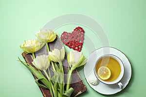 Blooming Saintpaulia, commonly known as African violet, cup of tea with lemon, vintage book close-up. Composition for