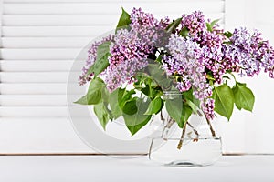 Blossom lilac flowers in glass vase on white shutters