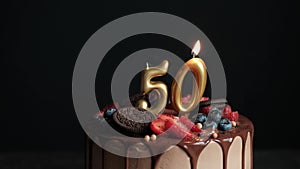 Blowing out candles on Chocolate birthday cake on black background with number fifty golden candles. Birthday cake for