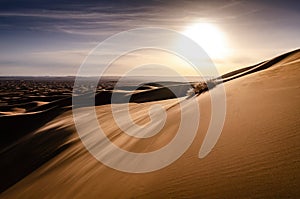 Blowing sand on top of a large sand dune in desert landscape. Early morning sunrise over the desert of Erg Chebbi. Silhouette.