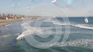 Blowing soap bubbles on ocean pier in California, blurred summertime background. Creative romantic metaphor, concept of