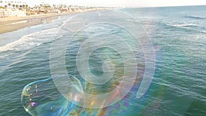 Blowing soap bubbles on ocean pier in California, blurred summertime background. Creative romantic metaphor, concept of dreaming