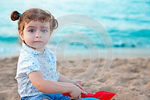 Blu eyes brunette toddler girl playing with sand in beach