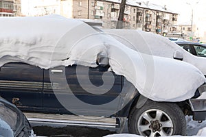 blue abandoned broken rusty car SUV parked by the road under a large layer of snow on a cold winter day