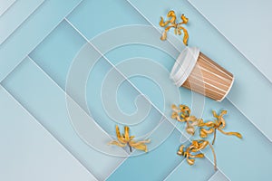 On a blue, abstract background, dry yellow flowers and a paper cup from under the coffee. Nice layout, there is a place for text.