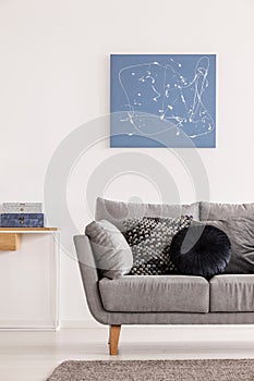 Blue abstract painting on white wall of contemporary living room interior with grey settee with pillows