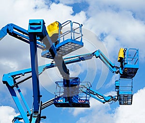 Blue aerial platform of cherry pickers up in the air against blue sky and clouds photo