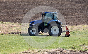 blue agricultural tractor without driver stands on a green meadow in front of a plowed field in the background  sunshine  during