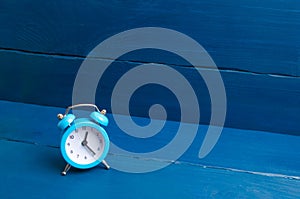 Blue alarm clock on a blue wooden background. The concept of time. Translation of hours for winter or summer time.
